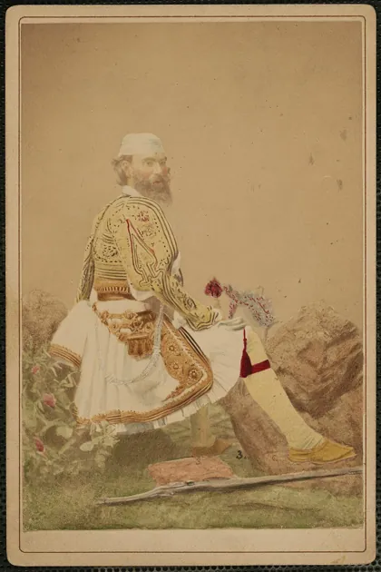 Bearded man in Grecian costume with rifle at feet, by P. Moraites & Co., photogr, 1878